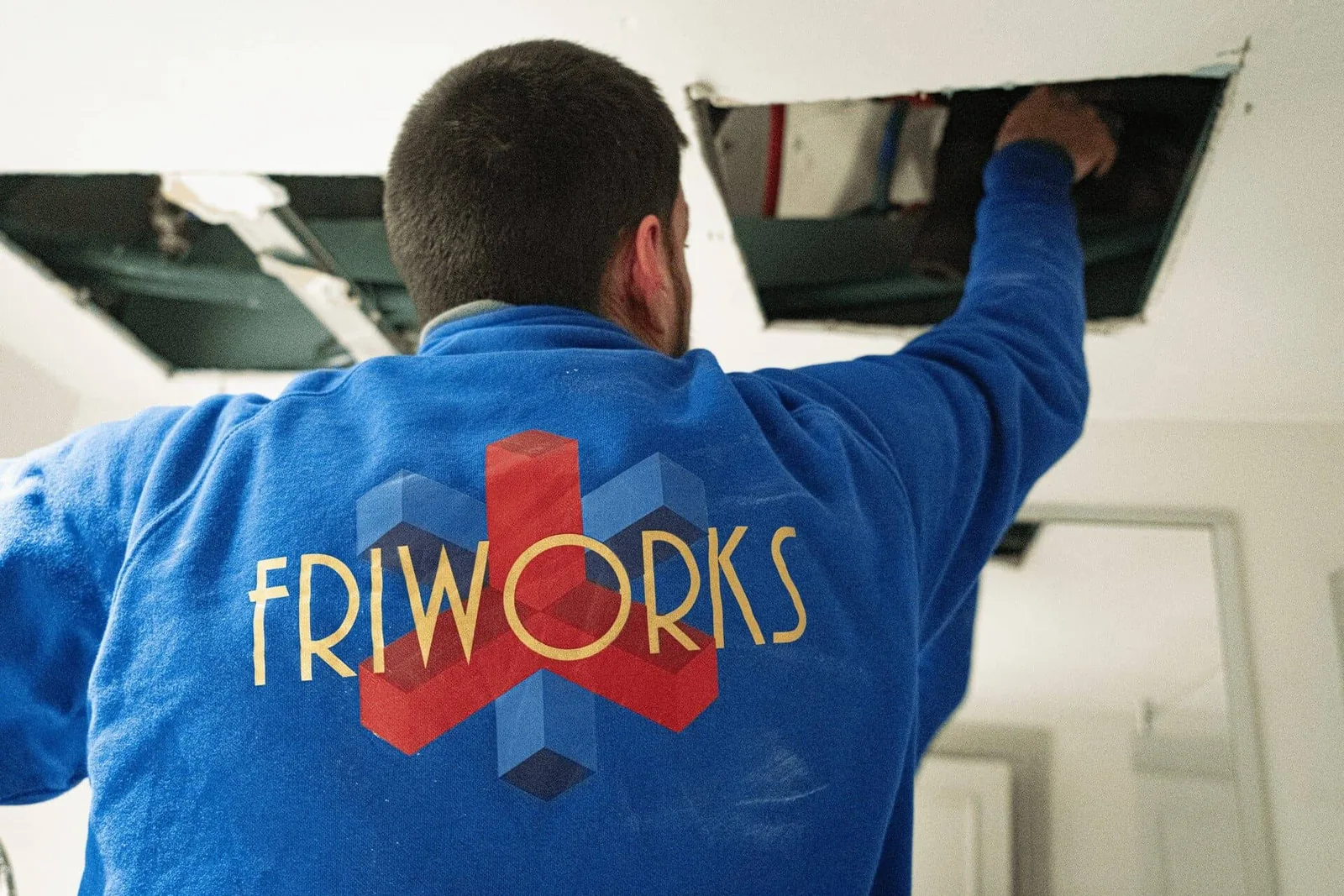 Técnico de Friworks, de espaldas y con el logotipo de la empresa, trabajando sobre un falso techo durante una instalación de climatización